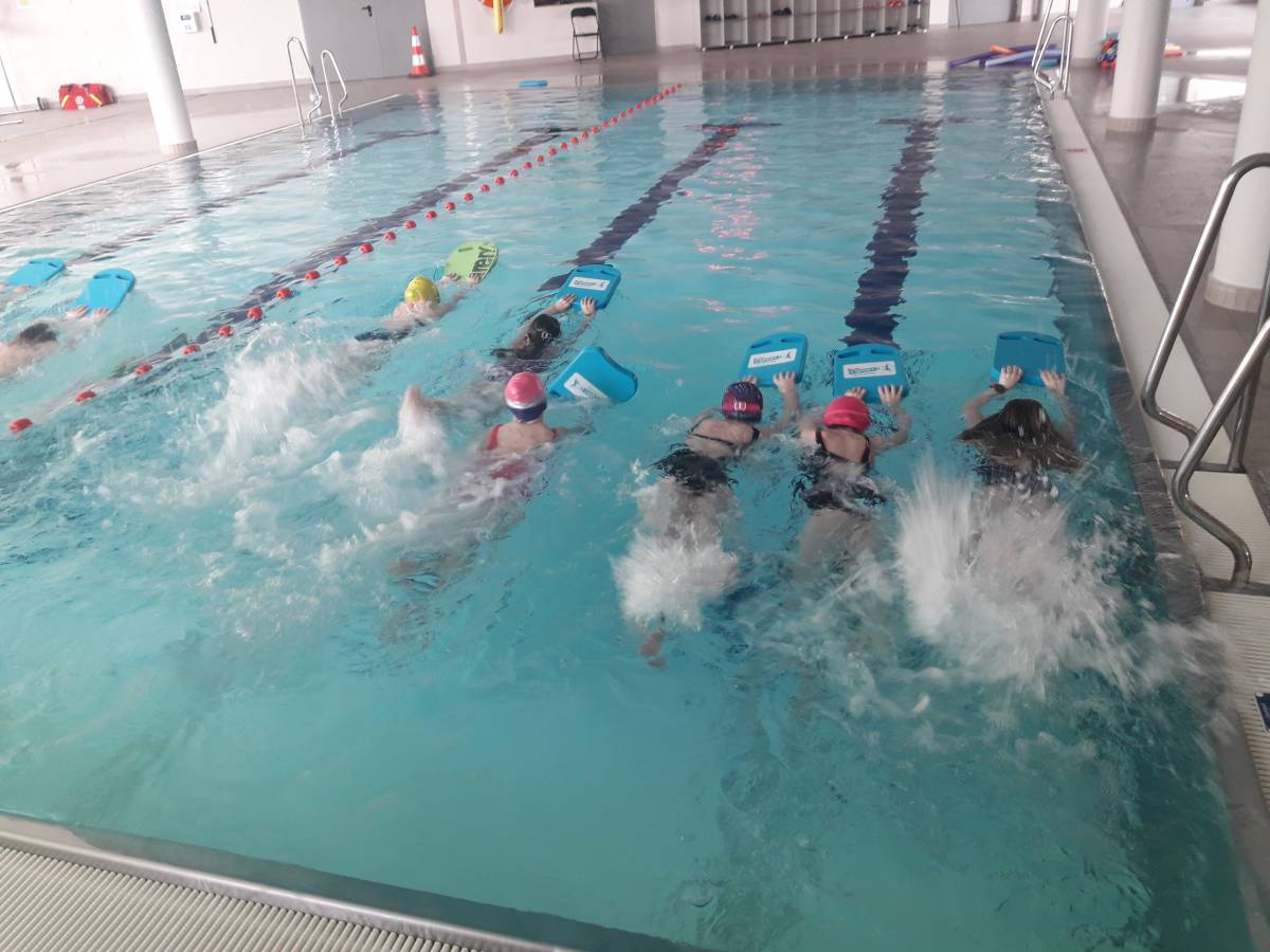 Dzieci ze styropianowymi deskami na basenie podczas nauki pływania