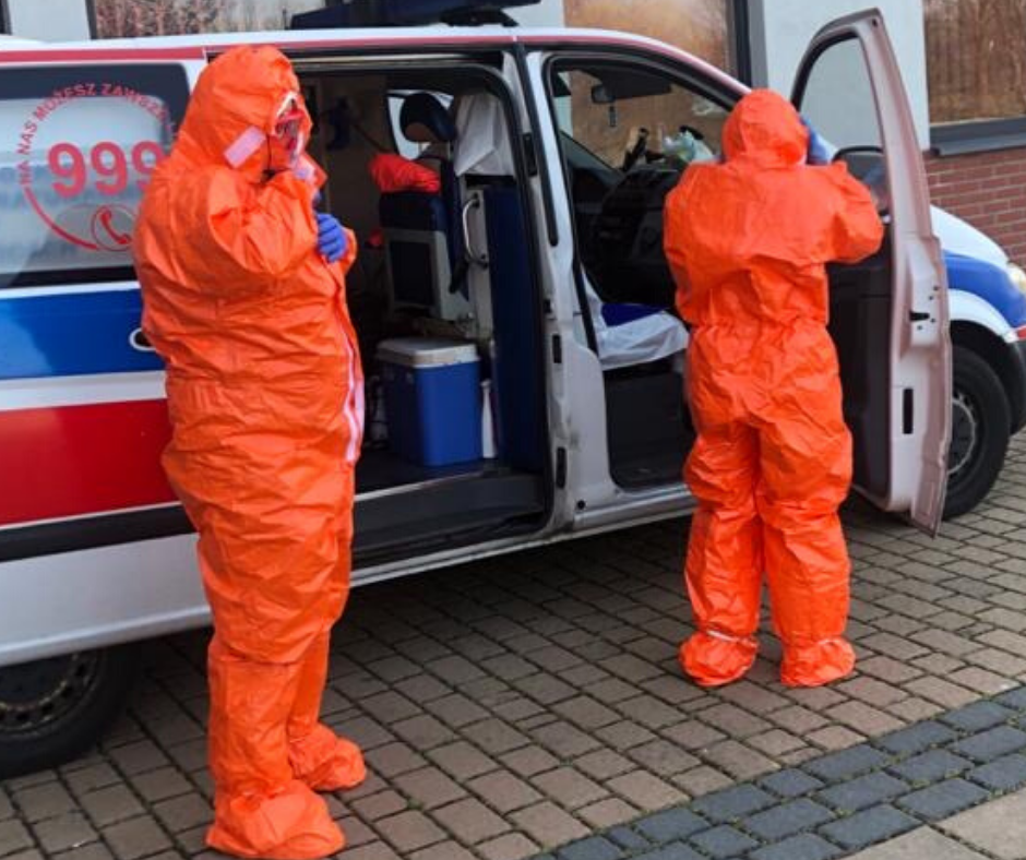 Zdjęcie dwóch pracowników służb medycznych w całości ubranych w kaftany ochronne