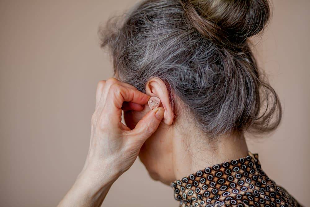 zdjęcie tyłu głowy starszej kobiety trzymającej rękę na aparacie słuchowym