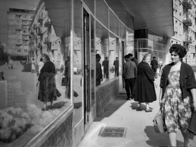 Zdjęcie przestawające kobietę przechodzącą obok wystawy sklepowej. Fotografia czarno-biała z archiwum Muzeum Miejskie w Tychach, z roku 1962.