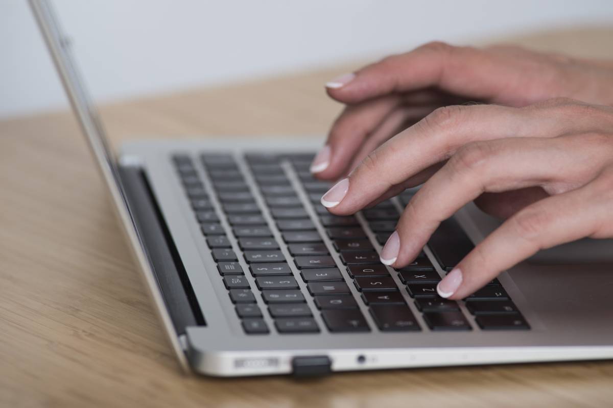 Zdjęcie kobiecych dłoni na klawiaturze laptopa.