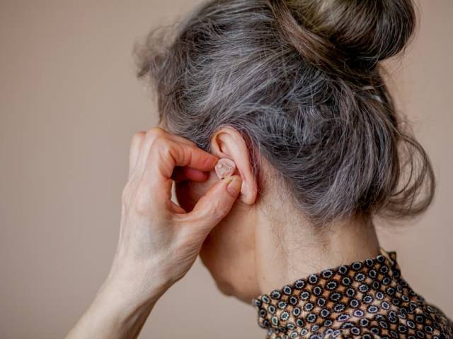 zdjęcie tyłu głowy starszej kobiety trzymającej rękę na aparacie słuchowym