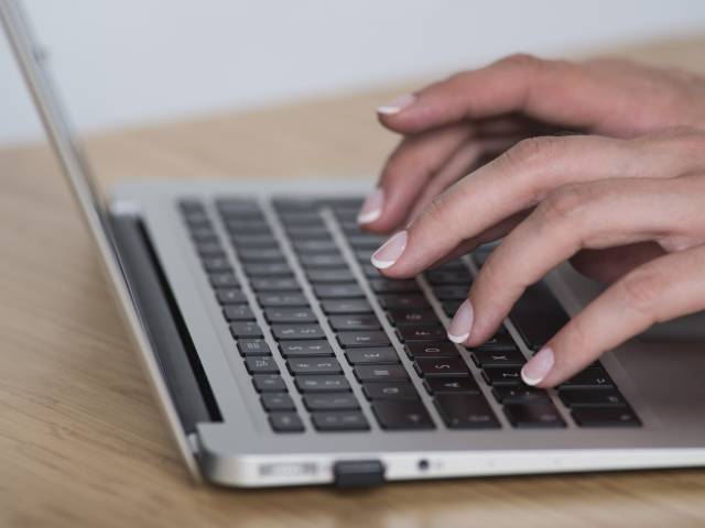 Zdjęcie kobiecych dłoni na klawiaturze laptopa.