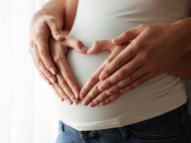 Zdjęcie dłoni przyszłych rodziców na brzuchu kobiety w ciąży, układających się w serce.