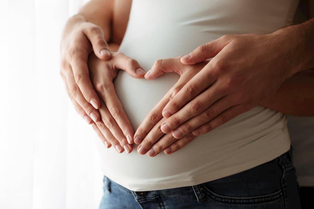 Zdjęcie dłoni przyszłych rodziców na brzuchu kobiety w ciąży, układających się w serce.