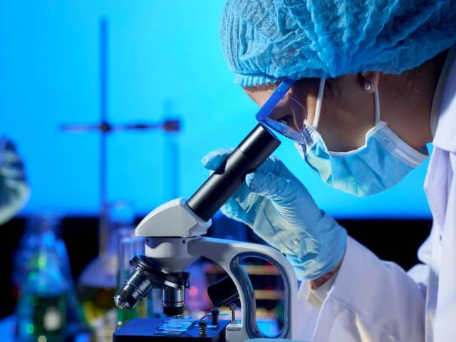 Zdjęcie - postać osoby pracującej w laboratorium spoglądającej na próbkę pod mikroskopem
