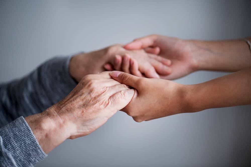 Zdjęcie - dłonie młode człowieka trzymające dłonie starszej osoby.