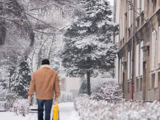 Zima w mieście - zdjęcie przedstawiające zaśnieżony chodnik i sylwetkę mieszkańca.