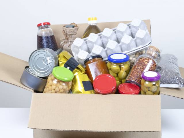 Pudełko wypełnione żywnością: puszki, wytłoczka z jajkami, słoik z oliwkami