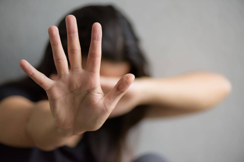 Na pierwszym planie dłoń kobiety w geście zatrzymującym przemoc, sylwetka kobiety nieostra. Autor: Freepik