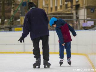 Mężczyzna i dziecko na łyżwach na lodowisku sezonowym