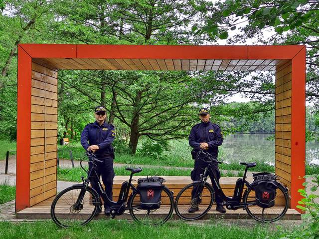 Tyscy strażnicy miejscy na tle ławki w Parku Północnym w Tychach