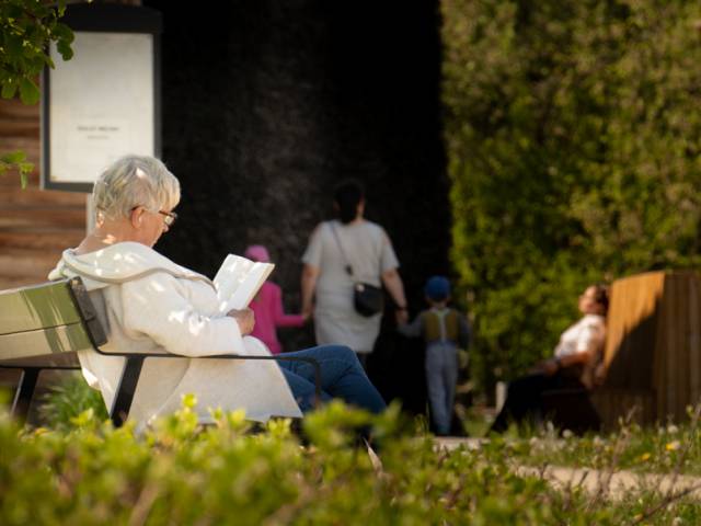Kobieta siedząca na ławce i czytająca książkę a Parku bł. Karoliny przy tężni