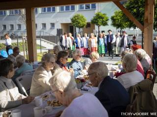 Pensjonariusze i pracownicy siedzący przy stołach podczas obchodów 40-lecia Dziennego Domu Opieki Społecznej "Wrzos". W tle zespół Urbanowiczanki.