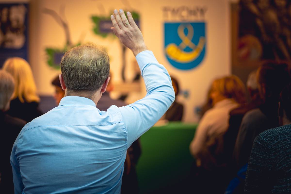 Mieszkaniec Tychów stoi tyłem i podnosi rękę podczas spotkania na temat OZE