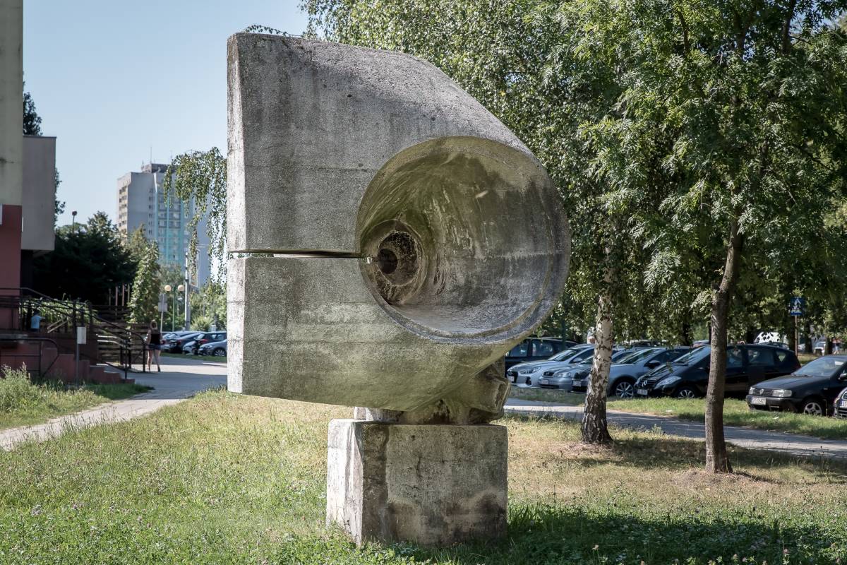 Rzeźba na tle drzew, samochodów i bloków mieszkalnych. 