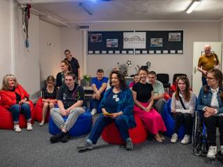 Kobiety, mężczyźni i dzieci siedzą na pufach i rozmawiają.