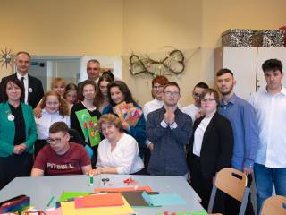 Dwóch mężczyzn, pięć kobiet i grupa dzieci uśmiechają sie do zdjęcia w sali lekcyjnej.