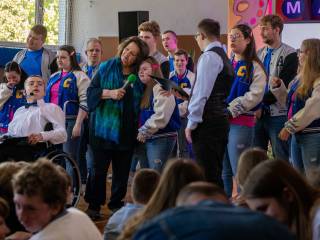 Kobieta z mikrofonem przytula się do dziewczynki, wokół nich dzieci z Zespołu Szkół Specjalnych na sali gimnastycznej.