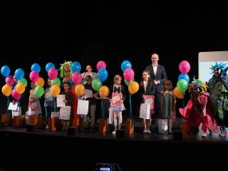 Dwóch mężczyzn, kobieta i grupa dzieci z dyplomami stoją na scenie w Teatrze.