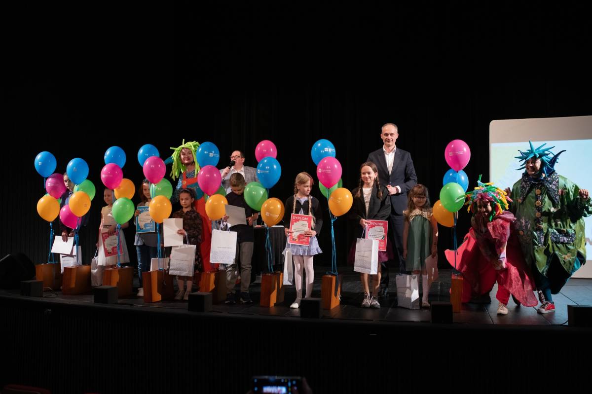 Dwóch mężczyzn, kobieta i grupa dzieci z dyplomami stoją na scenie w Teatrze.