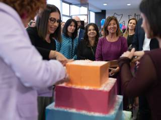 Grupa ludzi stoi wokół tortu, wszyscy się cieszą i świętują. 