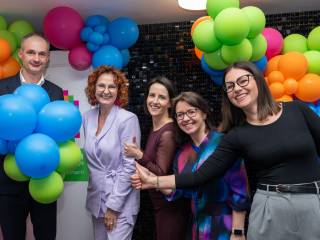 Cztery kobiety i mężczyzna stoją na tle balonów i śmiechają się do zdjęcia.