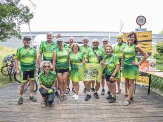 Grupa rowerzystów w zielonych strojach sportowych pozuje do zdjęcia na tle budynku, obok nich leżą rowery i widoczne są banery z napisem "Metrogra".