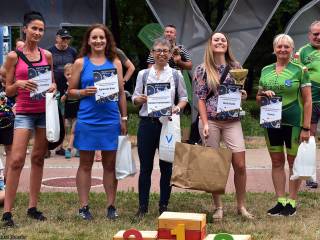 Pięć kobiet w sportowych strojach stoi z dyplomami i uśmiecha się do zdjęcia, w tle fragment napisu "Tychy" i park.
