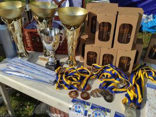 Nagrody leżą na białym stoliku: puchary, medale, bidony i kosz.