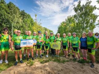 Duża grupa ludzi w sportowych zielonych strojach stoi z nagrodami i uśmiecha się do zdjęcia, w tle widać las.