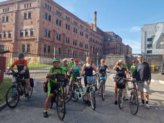 Grupa rowerzystów pozuje do zdjęcia na tle ceglastego budynku Browaru Tyskiego