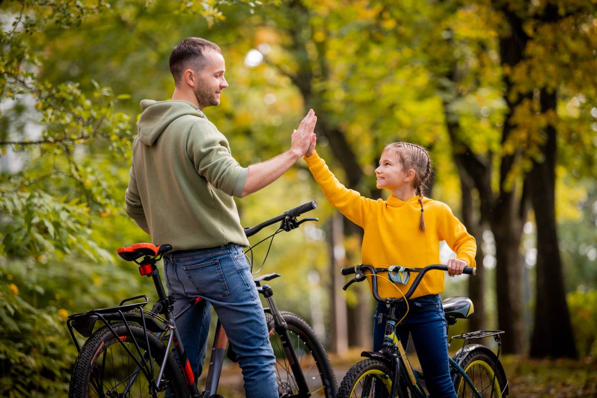 Rodzic z dzieckiem na rowerach, przybijają sobie piątkę.