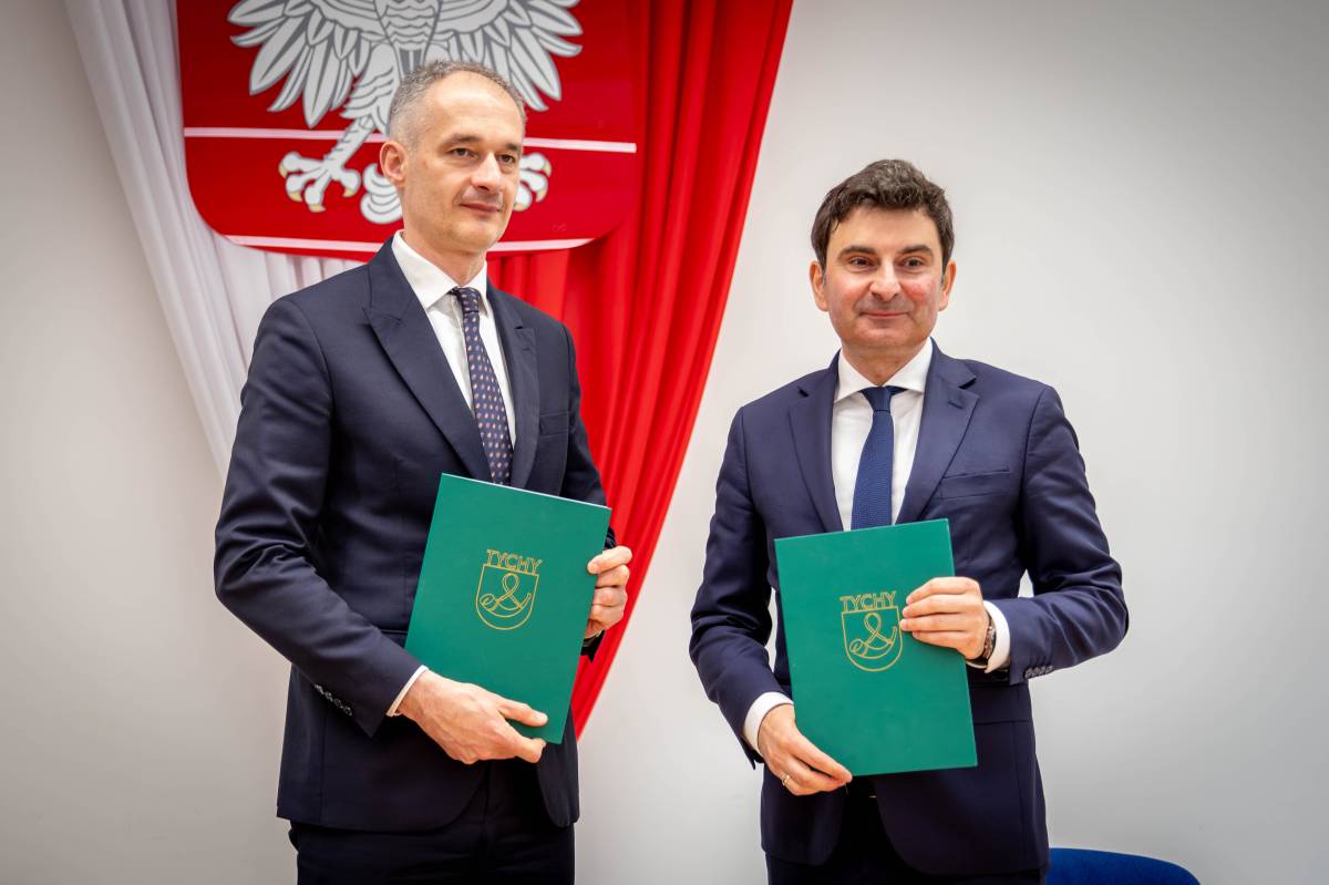 Dwóch mężczyzn trzyma umowę na dofinansowanie przebudowy i stoi na tle godła Polski