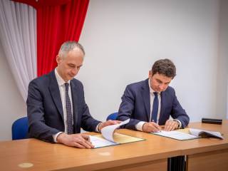 Prezydent miasta z Wojewodą Śląskim, Markiem Wójcikiem podpisują umowę na dofinansowanie przebudowy i siedzą przy biurku na tle godła polskiegiego.