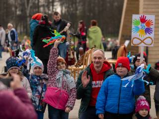 Siedmioro dzieci i mężczyzna uśmiechają się do zdjęcia, za nimi pomnik i przechodzący ludzie.