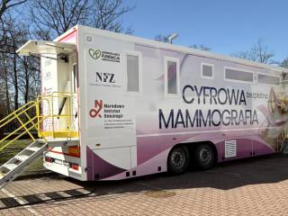 Różowo-biały mammobus z napisem "Cyfrowa mammografia". W tle widać drzewa i budynek.