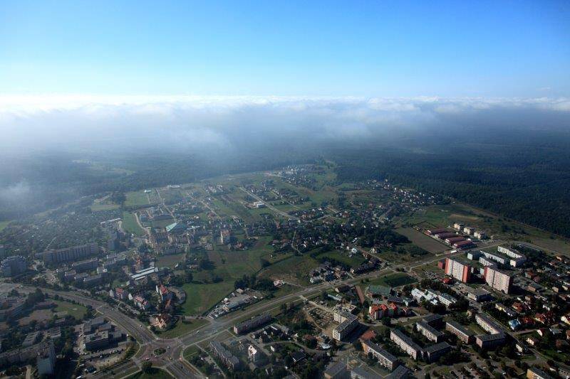 Widok z drona na miasto — widoczne są domy, ulice i las.