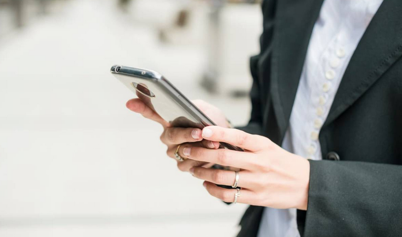 Kobieta w marynarce i niebieskiej koszuli trzyma telefon w ręce na białym tle.